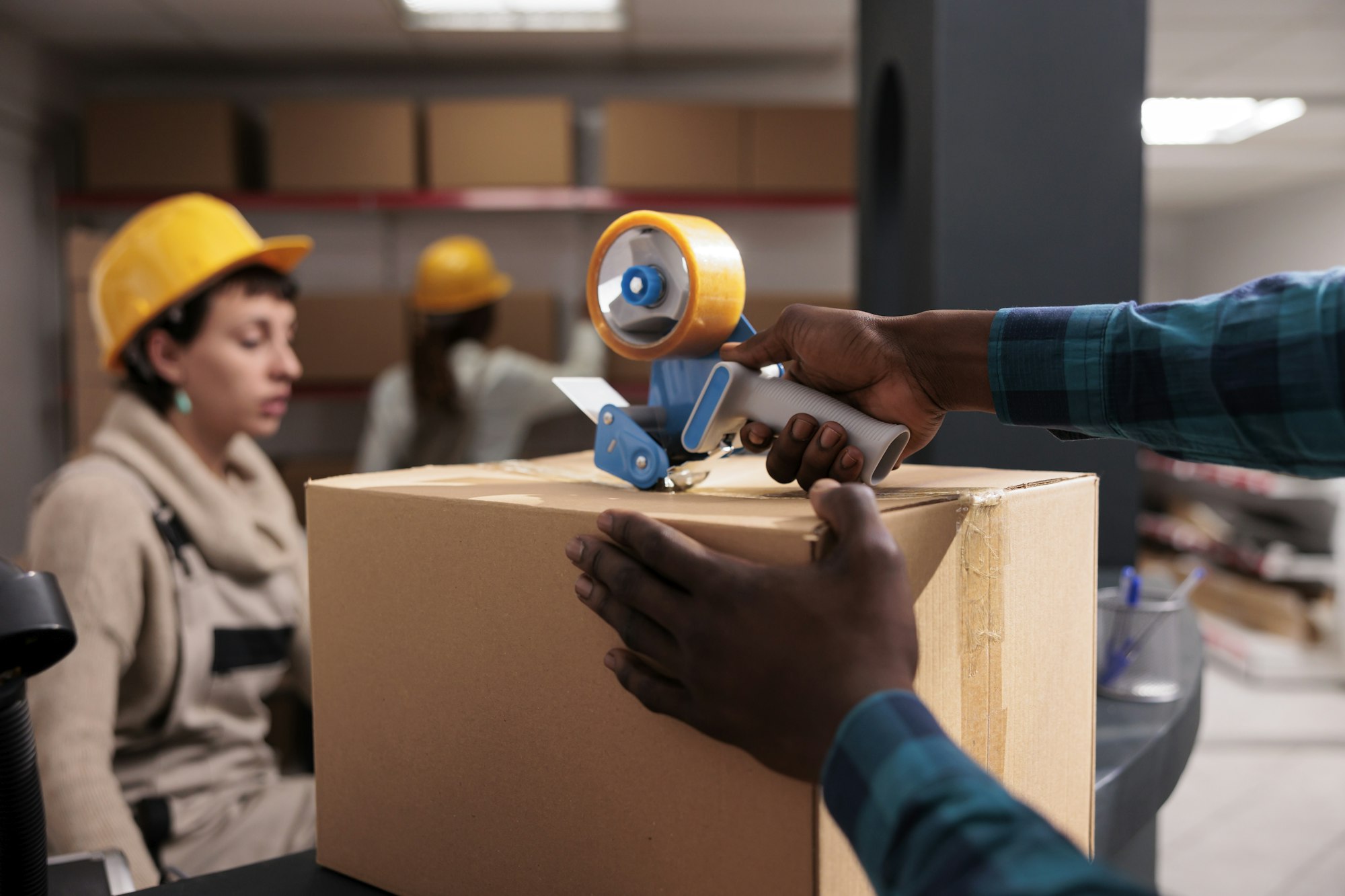 African american warehouse worker packing parcel with adhesive dispenser