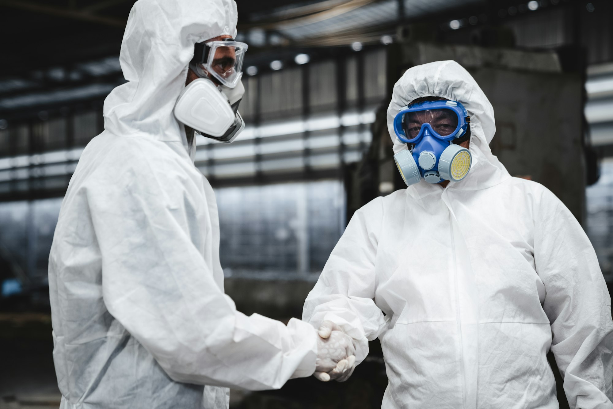 Workers in protective suits inspect chemicals in an old factory, safeguarding against hazards.